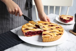 Woman cutting tasty cherry pie at white marble table, closeup