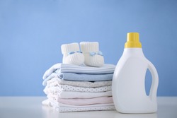 Detergent and children's clothes on white table near blue wall