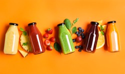 Flat lay composition with bottles of delicious juices and fresh ingredients on orange background