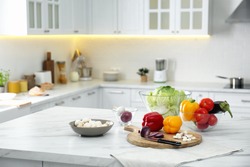 Different fresh vegetables and mushrooms on white table in modern kitchen. Space for text