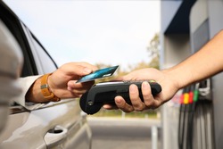 Man sitting in car and paying with credit card at gas station, closeup