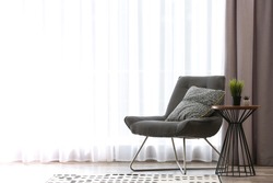Comfortable chair near window with elegant curtains in room. Space for text