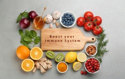 Set of natural products and wooden board with text Boost Your Immune System on grey table, flat lay