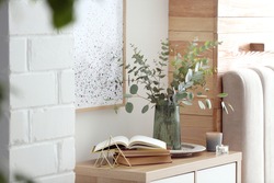 Beautiful eucalyptus branches and books on cabinet in modern room. Interior design
