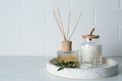 Candles, eucalyptus branch and aromatic reed air freshener on white table near brick wall, space for text. Interior elements