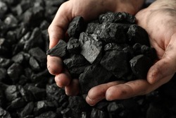 Man holding coal in hands over pile, closeup