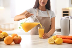 Young woman pouring tasty fresh juice into glass at table in kitchen, closeup