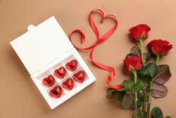 Box of heart shaped chocolate candies and bouquet on brown background, flat lay