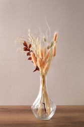 Dried flowers in vase on wooden table against light background
