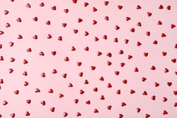 Red heart shaped sprinkles on pink background, flat lay