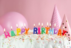 Birthday cake with burning candles on pink background, closeup