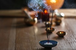 Incense sticks smoldering on wooden table in room. Space for text