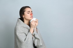 Young woman with blanket sneezing on light grey background, space for text. Runny nose