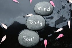 Stones with words Mind, Body, Soul and flower petals in water, flat lay. Zen lifestyle