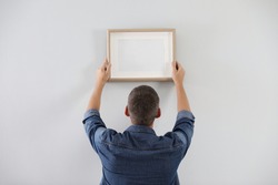 Man hanging picture on white wall indoors. Interior decoration