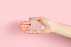 Woman with rose quartz gua sha tool on pink background, closeup