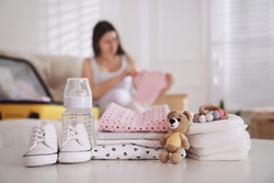 Baby clothes with accessories on white table and pregnant woman packing suitcase for maternity hospital indoors