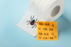 Toilet paper roll with drawn spider and words Ha-Ha  on light blue background. Celebrating April Fool's Day