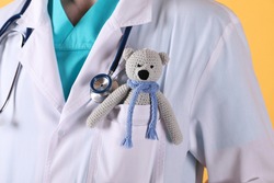 Pediatrician with toy bear and stethoscope on yellow background, closeup