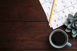 Sudoku, pencil, cup of coffee and decorative succulent on wooden table, flat lay. Space for text
