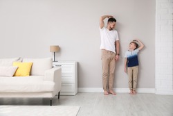 Father and son comparing their heights near wall in living room