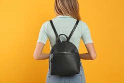 Woman with stylish backpack on yellow background, back view