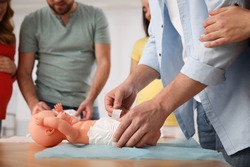 Future fathers and pregnant women learning how to swaddle baby at courses for expectant parents indoors, closeup