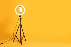 Modern tripod with ring light and smartphone on yellow background. Space for text
