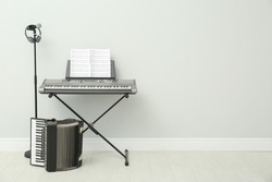 Electronic synthesizer, accordion and microphone near white wall indoors, space for text. Musical instruments