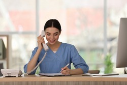 Receptionist talking on phone at countertop in hospital