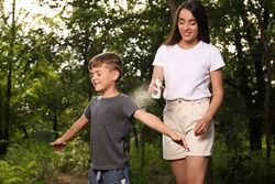 Woman applying insect repellent on her son's arm in park. Tick bites prevention
