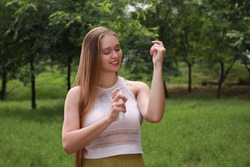 Woman applying insect repellent onto arm in park. Tick bites prevention