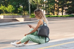 Young woman with stylish backpack and smartphone on stairs outdoors