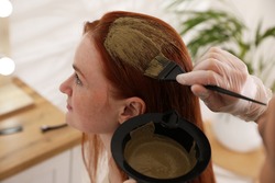 Professional hairdresser dyeing woman's hair with henna in beauty salon