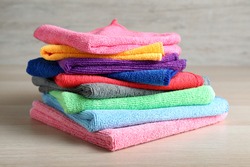 Stack of colorful microfiber cloths on light wooden table, closeup
