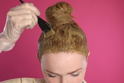 Young woman dyeing her hair with henna on pink background, closeup