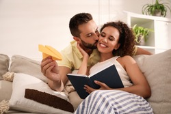 Happy man playing with paper plane while his girlfriend reading book in living room, focus on hand