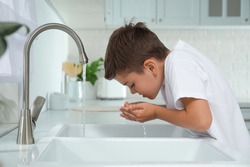 Boy drinking tap water over sink in kitchen