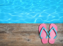 Pair of flip flops on wooden deck near swimming pool, top view  