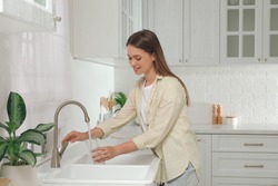 Woman filling glass with water from tap in kitchen