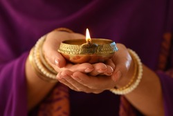 Woman holding lit diya lamp in hands, closeup. Diwali celebration