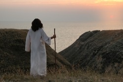Jesus Christ with stick on hills at sunset, back view. Space for text