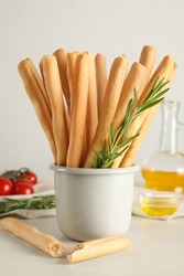 Delicious grissini sticks, oil, rosemary and tomatoes on white wooden table