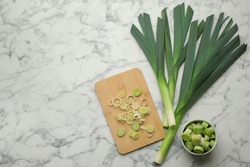 Whole and cut fresh leeks on white marble table, flat lay. Space for text