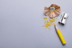 Yellow pencil, shaving, crumbs and sharpener on grey background, flat lay. Space for text