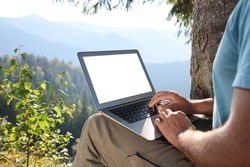Man working on laptop outdoors surrounded by beautiful nature, closeup. Space for text