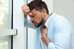 Man suffering from pain during breathing near window
