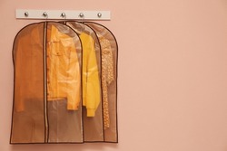 Garment bags with clothes hanging on light wall. Space for text