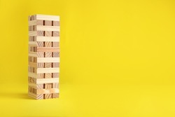 Jenga tower made of wooden blocks on yellow background, space for text