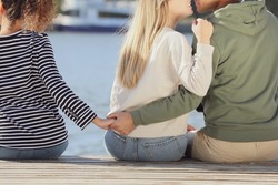 Man holding hands with another woman behind his girlfriend's back on pier near river, closeup. Love triangle